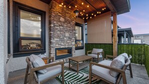 An outdoor patio with stone walls, a fireplace, wicker furniture, and string lights. - YVR/Luxe/Theatre/AC/New Westminster (New Westminster)