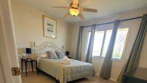 A bedroom with a bed, a ceiling fan, a bedside table with a lamp, a framed quote on the wall, and a window with curtains. - CASA Allegro - Active Vacationers Paradise (Sun City West)