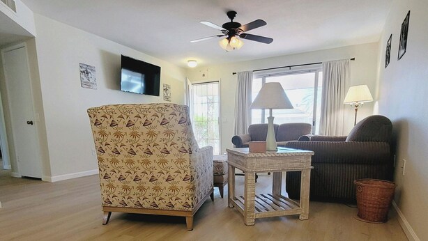 A living room with a patterned armchair, a small table, a ceiling fan, and a television mounted on the wall. - CASA Allegro - Active Vacationers Paradise (Sun City West)