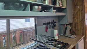 A compact kitchen with a gas stove, a kettle, and various pots and pans on shelves. - Mobile home N°17 (Fourmies)