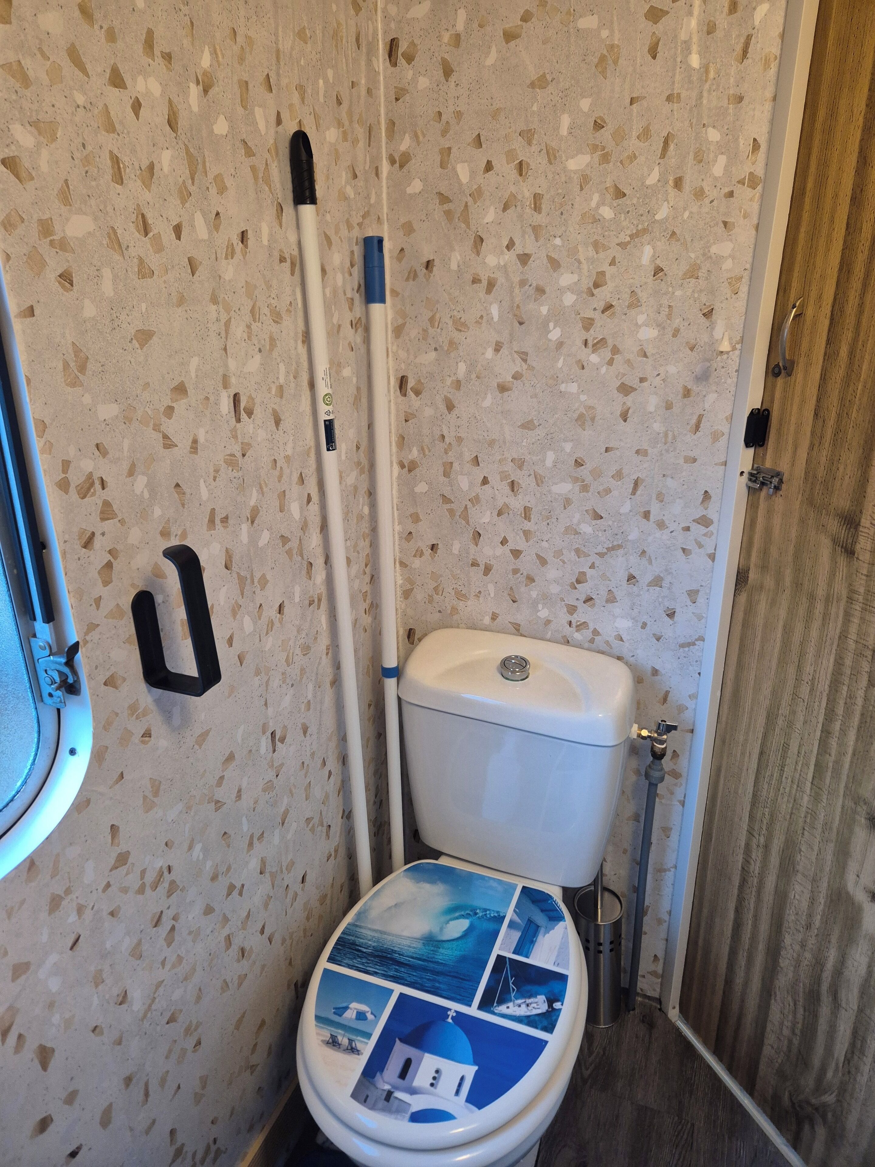 Kylpyhuone, jossa on valkoinen wc-istuin, moppi ja puuovi.