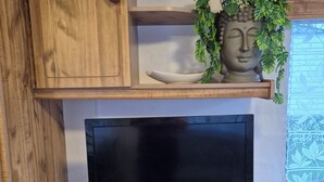 A wooden entertainment unit with a flat-screen TV, a remote control, and a decorative Buddha statue with plants. - Mobile home N°17 (Fourmies)