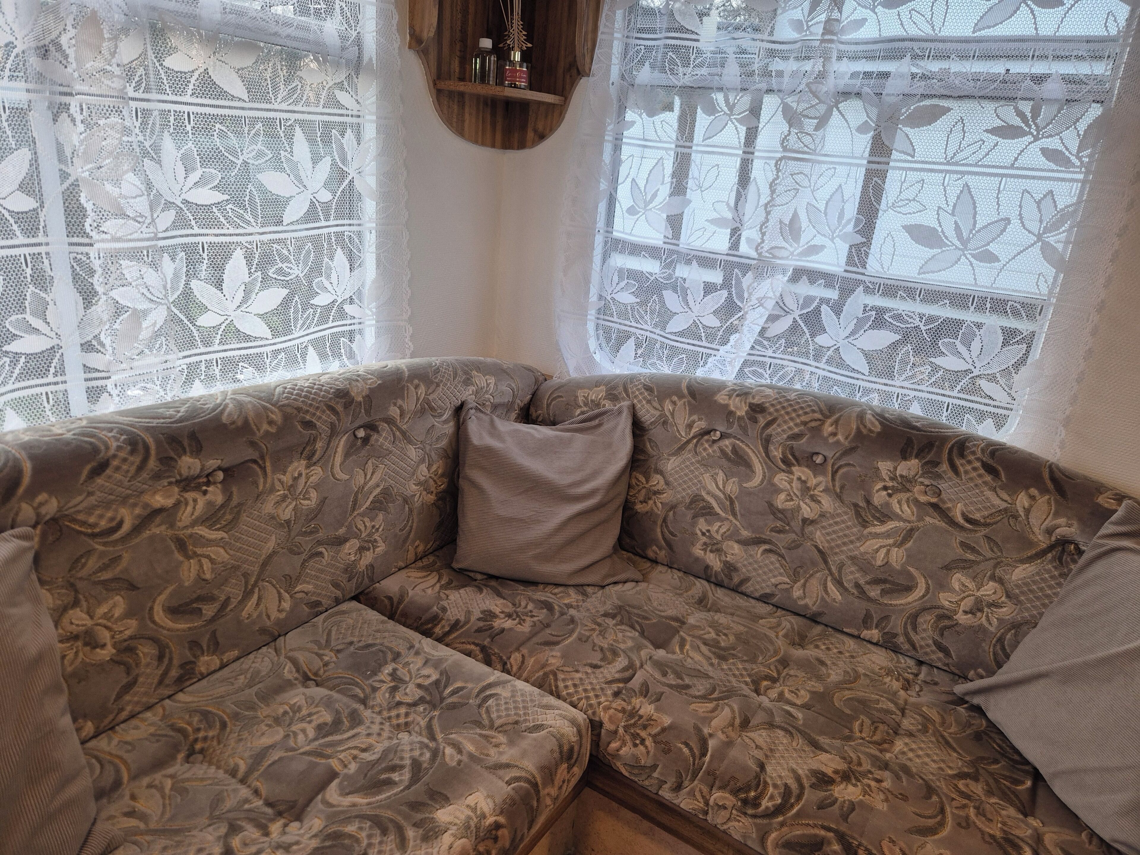 Ein Ecksofa mit Blumenmuster, ein Kissen und durchbrochenen Vorhängen.