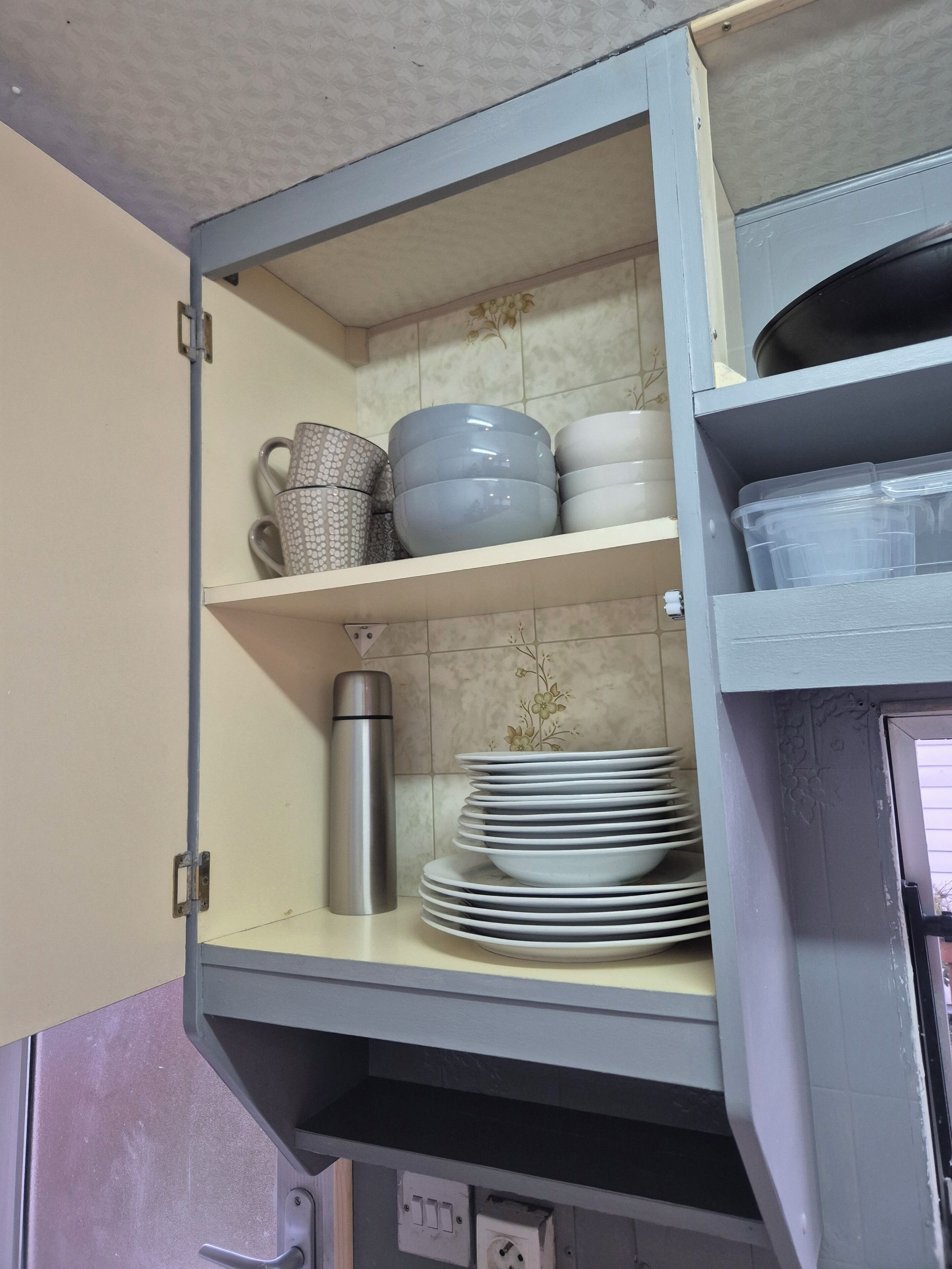 A kitchen cabinet with shelves containing plates, bowls, and a stainless steel water bottle.