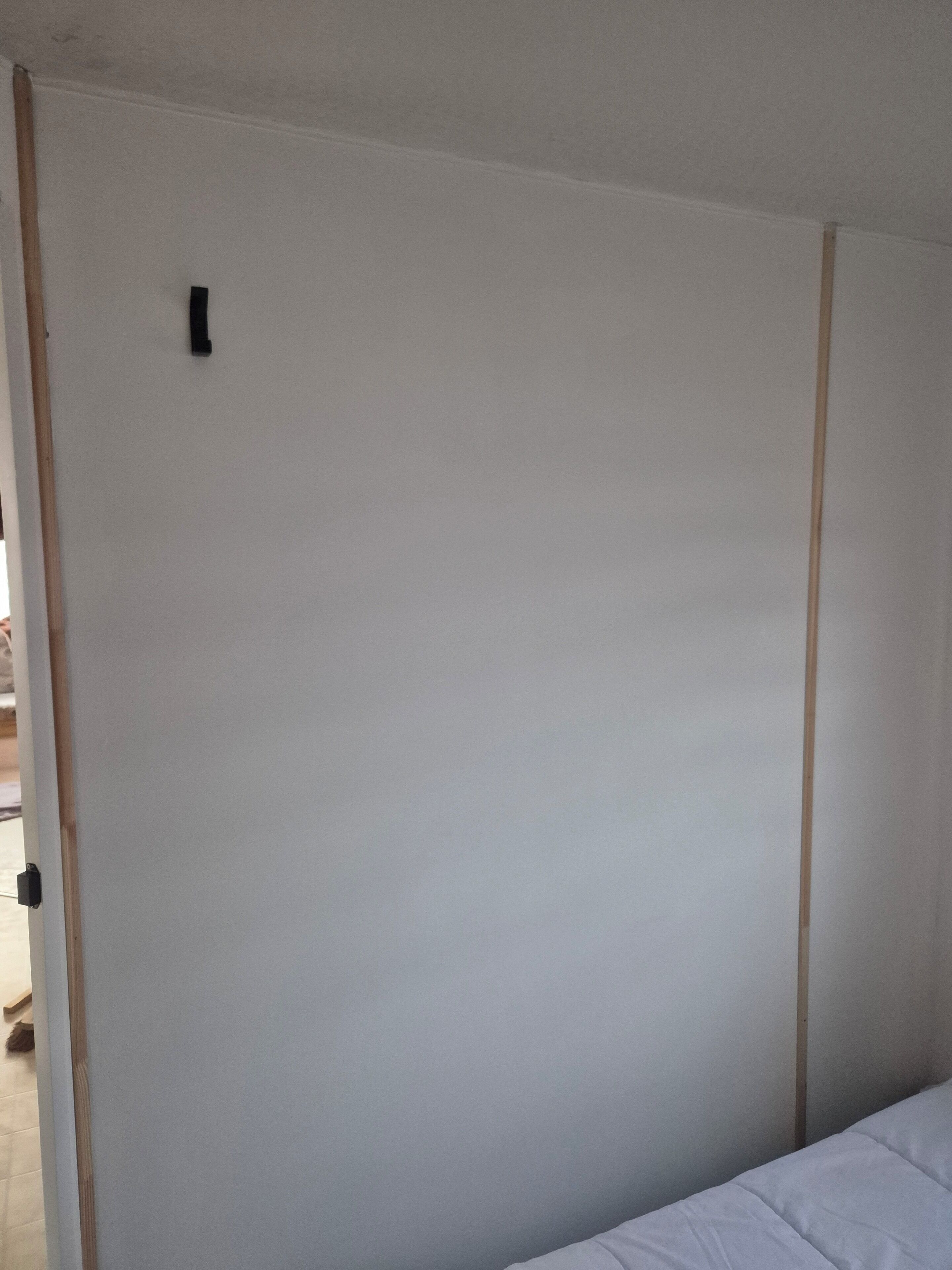 Um quarto com porta fechada, cama com roupa de cama branca e piso de madeira.