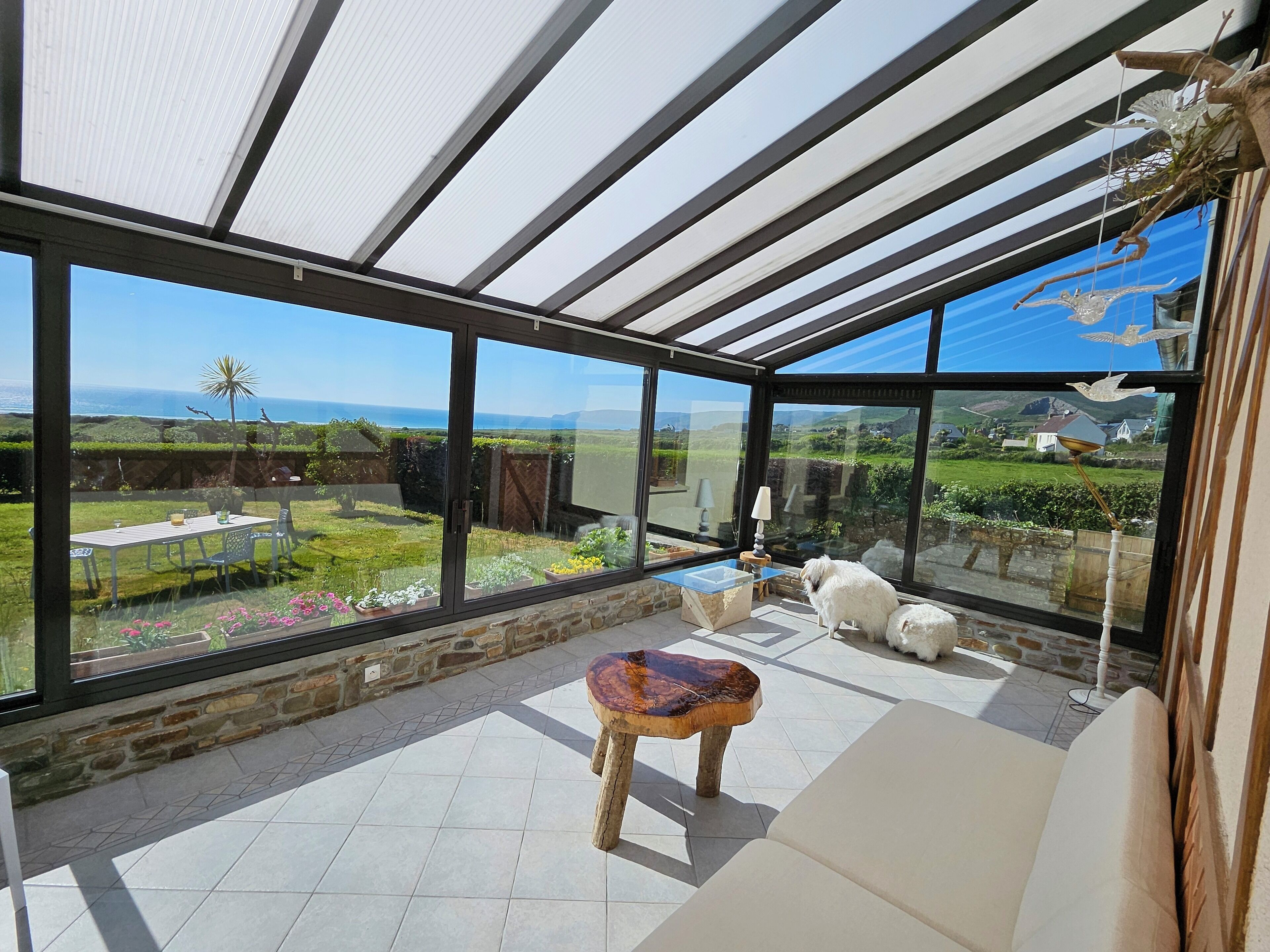 A conservatory with a glass ceiling, a stone wall, and a view of a garden and sea.