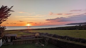 Zonsondergang vanaf een kustbezit met een klein huis, een omheind gazon en een grasveld.