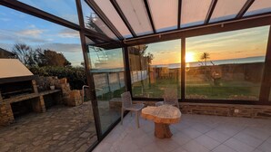 Een glazen patio met een stenen tafel en stoelen, met uitzicht op een tuin en een zonsondergang.