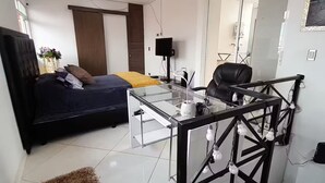 Una camera da letto moderna con un letto, una scrivania e una sedia. In parete, una TV e uno specchio.
