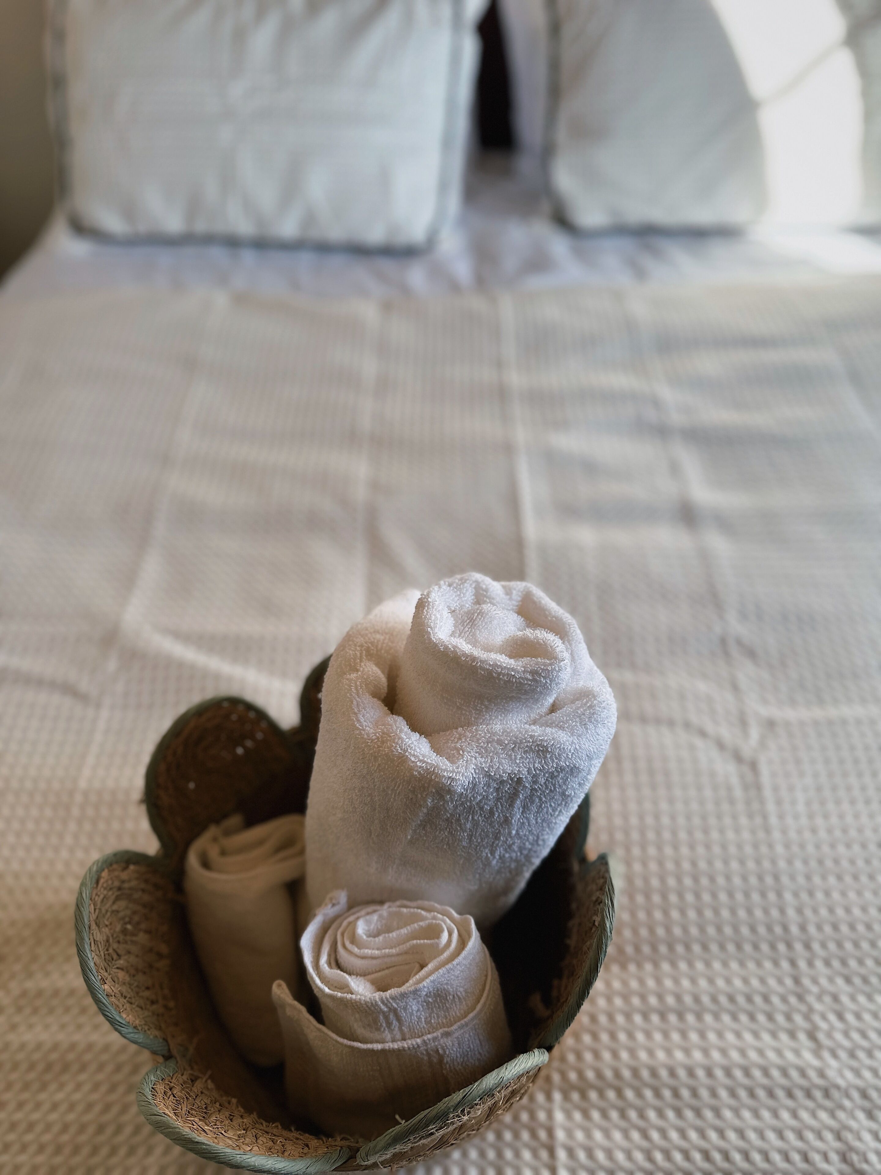 A neatly made bed with white linens and a basket of rolled towels.