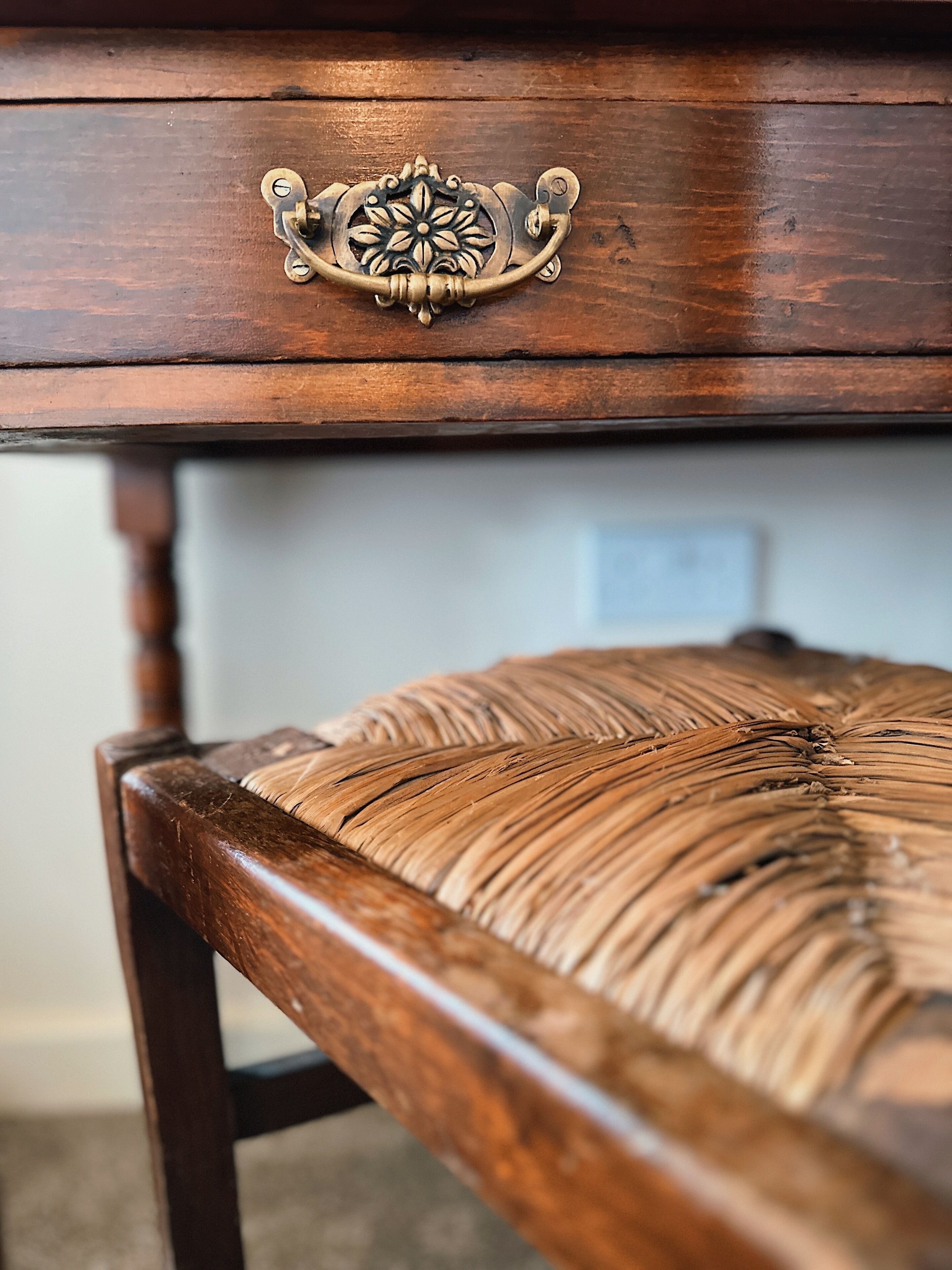 A wooden chair with a woven seat and a brass drawer handle.