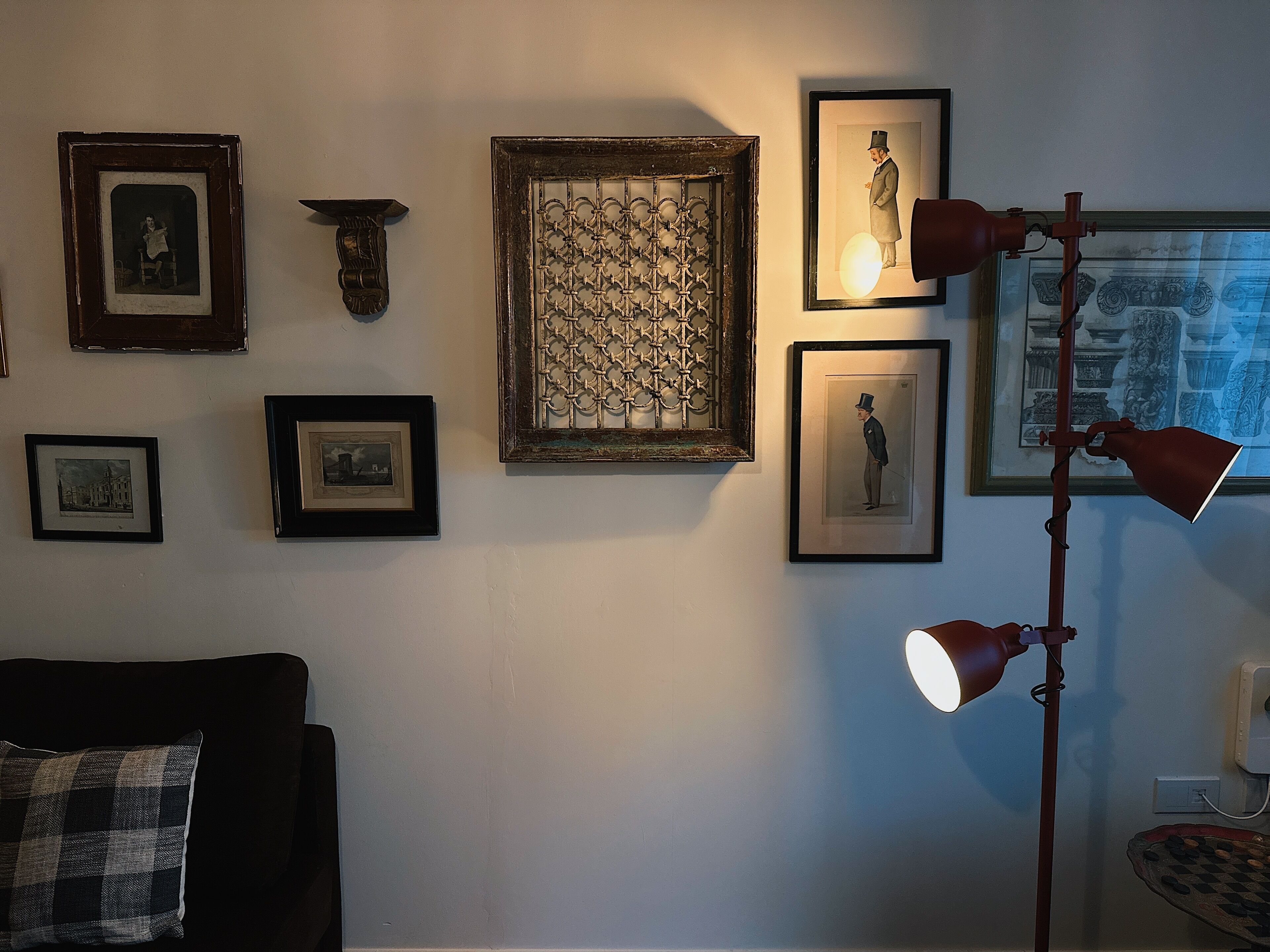 A room with a dark-colored sofa, a patterned wall hanging, and a floor lamp.