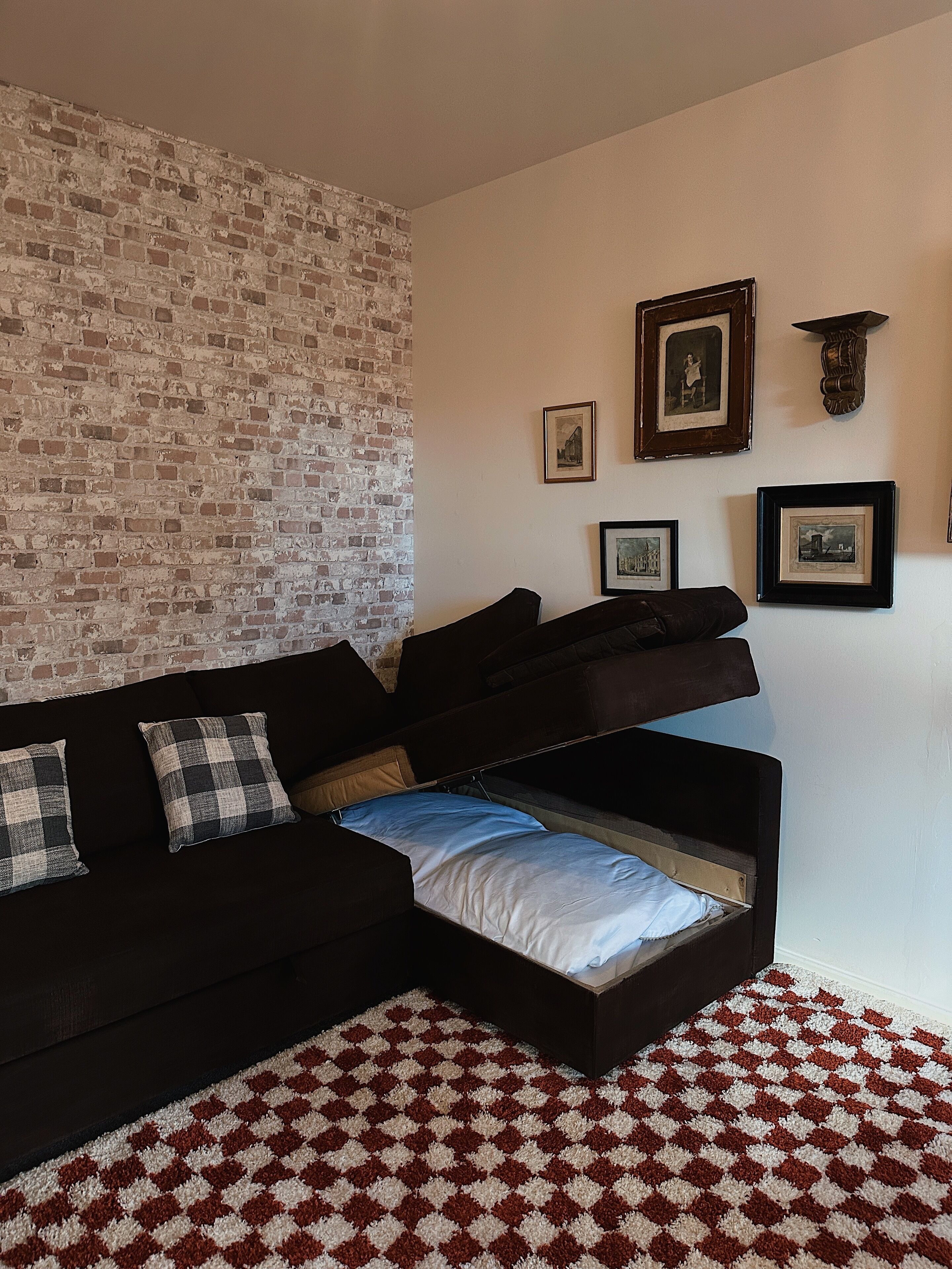 Un salon avec un canapé noir, un tapis à carreaux et un mur en briques.