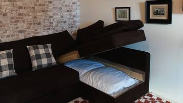 Un salon avec un canapé noir, un tapis à carreaux et un mur en briques.