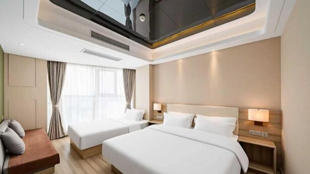 A hotel room with two beds, a sofa, a TV, and a window with curtains.