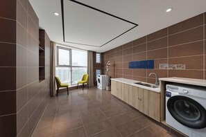 A modern kitchen with a washing machine, a sink, and a chair. - Xincheng Hotel (Yantai University International Expo Center Branch) (Yantai)