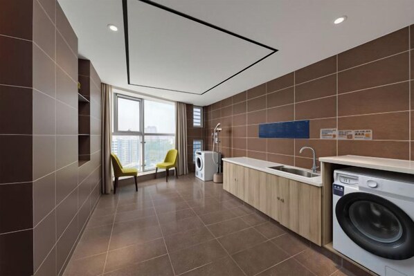 A modern kitchen with a washing machine, a sink, and a chair. - Xincheng Hotel (Yantai University International Expo Center Branch) (Yantai)