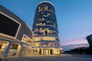 A modern hotel with a curved facade, multiple floors, and illuminated windows.