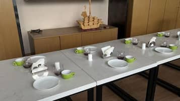 A long dining table with multiple sets of white and green plates, cups, and a ship model on a shelf above.