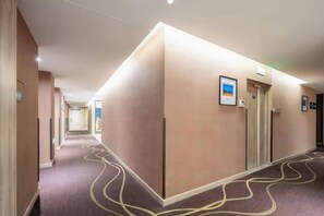 A hotel hallway with a carpeted floor, a door with a sign, and a light fixture. - Xincheng Hotel (Yantai University International Expo Center Branch) (Yantai)