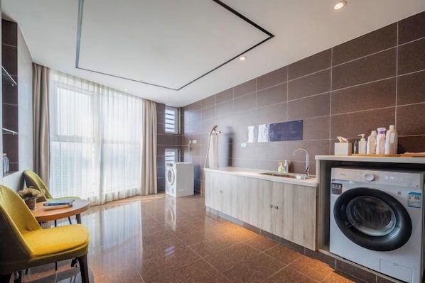 A modern hotel room with a kitchen area, including a washing machine, a dining table, and a chair.