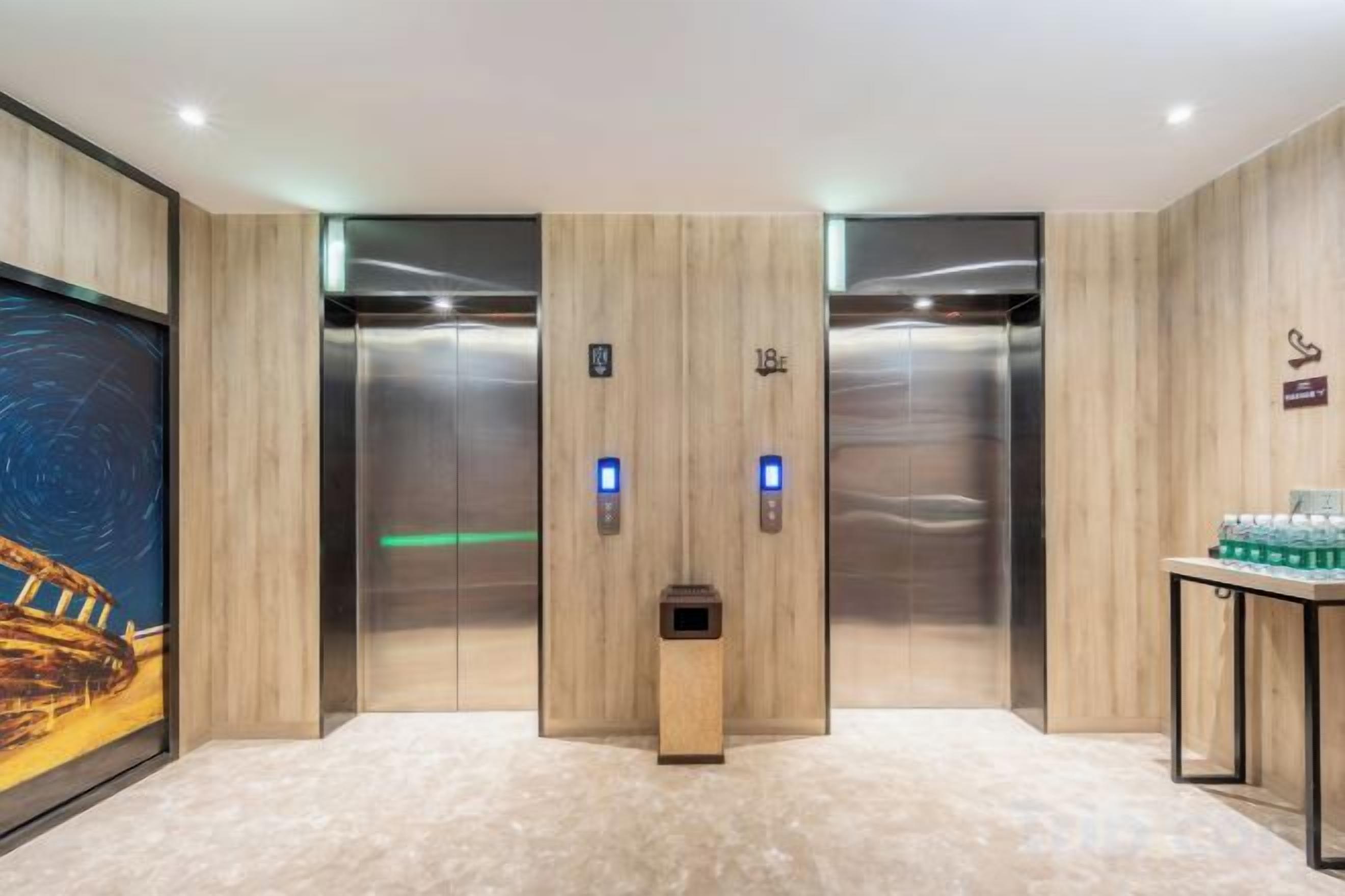 A modern elevator with two buttons, a digital display, and a small trash bin.