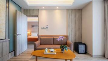 A modern hotel room with a wooden floor, a sofa, a coffee table with a tray, a potted plant, and a television.