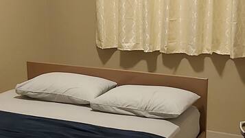A bedroom with a bed, a window with curtains, an air conditioning unit, and a bedside table.