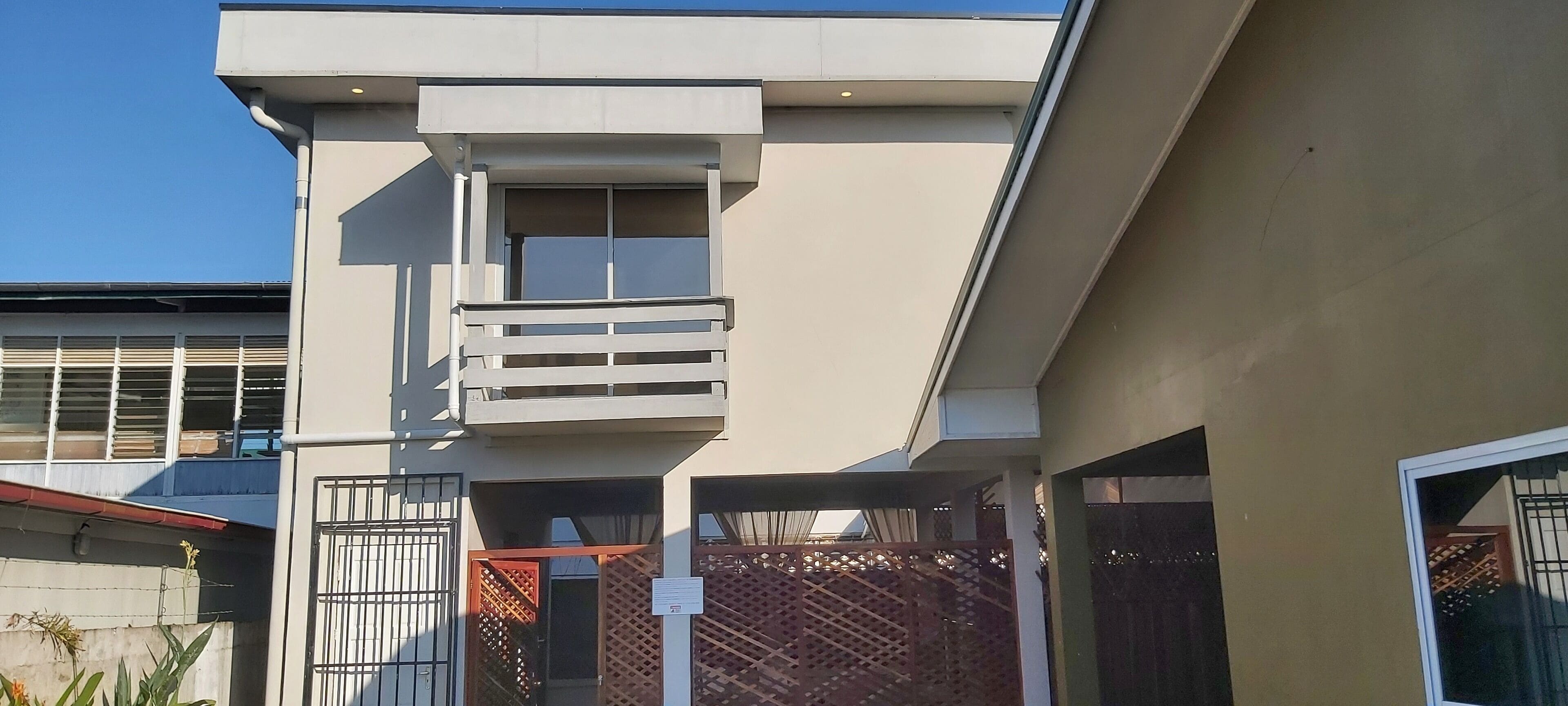 A modern building with a balcony, a gated entrance, and a clear sky.