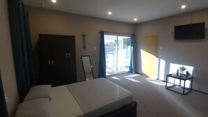 A room with a bed, a desk, a chair, a TV mounted on the wall, and a door leading outside. - Waterland Suites (Paramaribo)