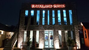 A building with a sign reading "Waterland Suites" at night, featuring a stone facade and multiple windows. - Waterland Suites (Paramaribo)
