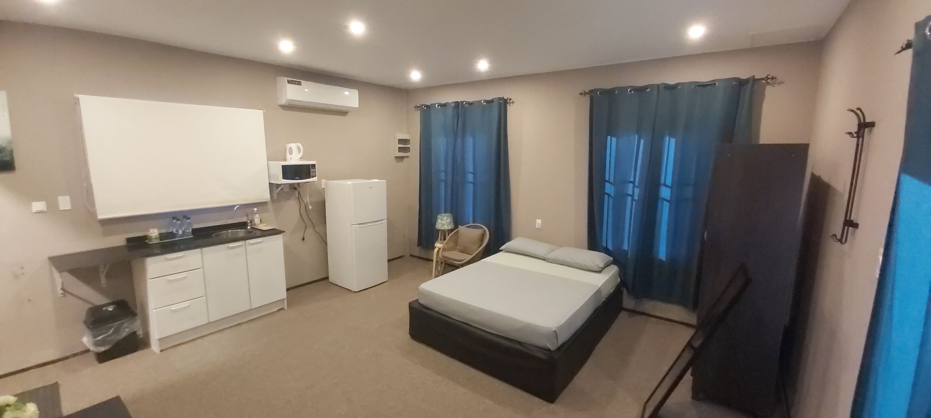 A compact hotel room with a bed, a small kitchenette, a chair, and a TV.