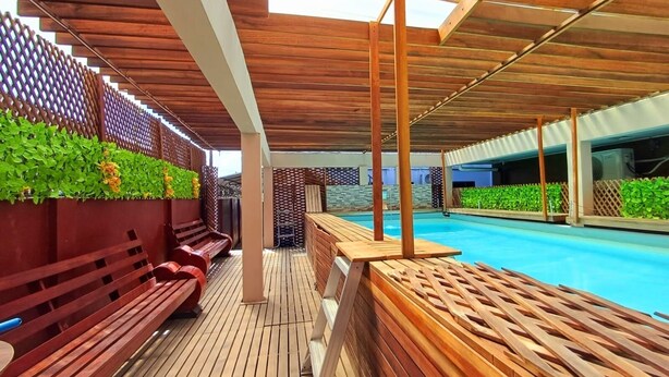 A wooden deck with a pool, wooden benches, and a wooden fence with greenery. - Waterland Suites (Paramaribo)