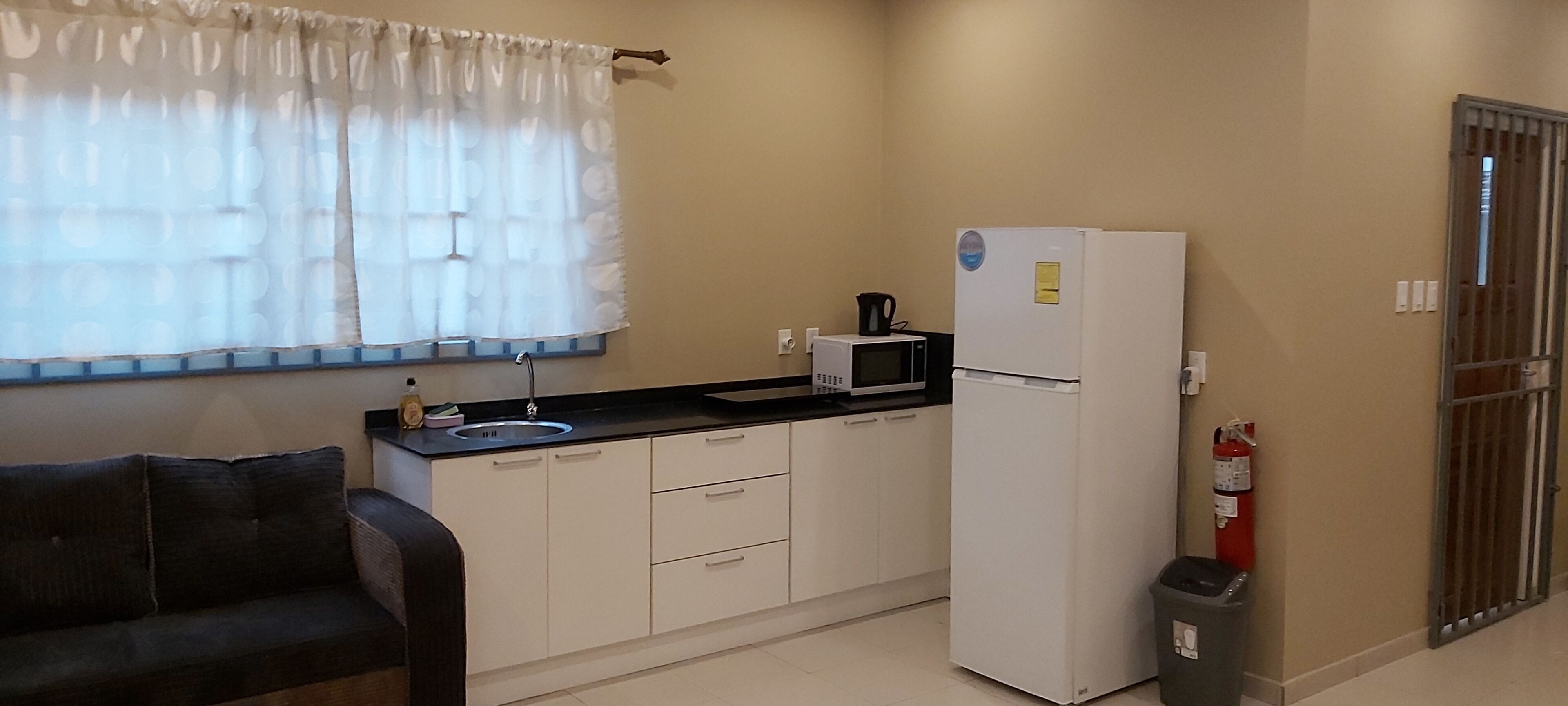 A compact kitchen with a refrigerator, microwave, sink, and a fire extinguisher.