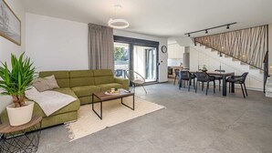 Moderni olohuone, jossa on vihreä sohva, sohvapöytä ja ruokailutila tuoleineen. Portaissa on ainutlaatuinen kaide, ja ne johtavat ylemmälle tasolle.