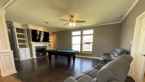 Ein geräumiges Wohnzimmer mit Pooltisch, einer gemütlichen grauen Couch und einem Kamin.