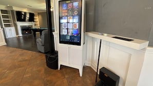 Ein digitales Kiosk mit Touchscreen, ein Billardtisch und ein Kamin in einem Raum mit Fliesenboden und weißen Wänden.