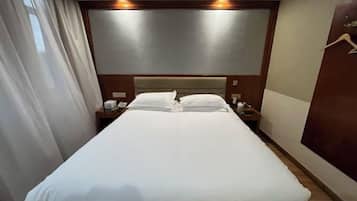 A hotel room with a large bed, bedside tables, a headboard, and a curtain.