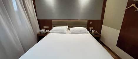 A hotel room with a large bed, bedside tables, a headboard, and a curtain.