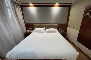 A hotel room with a large bed, bedside tables, a headboard, and a curtain.