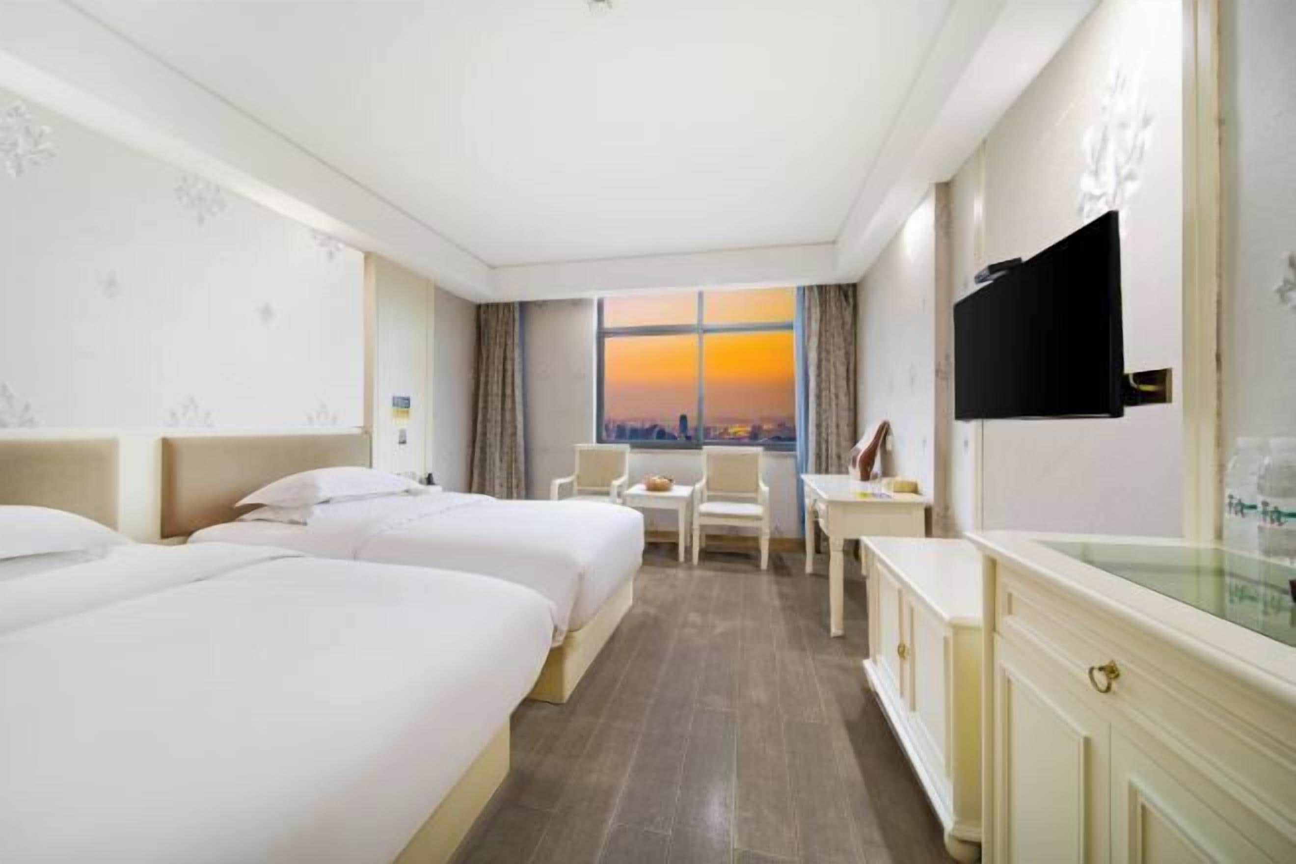 A hotel room with two beds, a desk, a chair, and a TV.