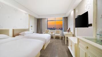 A hotel room with two beds, a desk, a chair, and a TV.