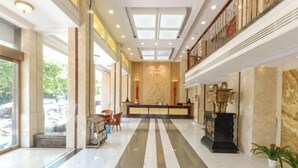 A hotel lobby with a central reception desk, a marble floor, and a staircase leading to an upper level. - NOMC Hotel (Xianju)