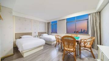 A hotel room with two beds, a dining table with chairs, and a cityscape view through the window.