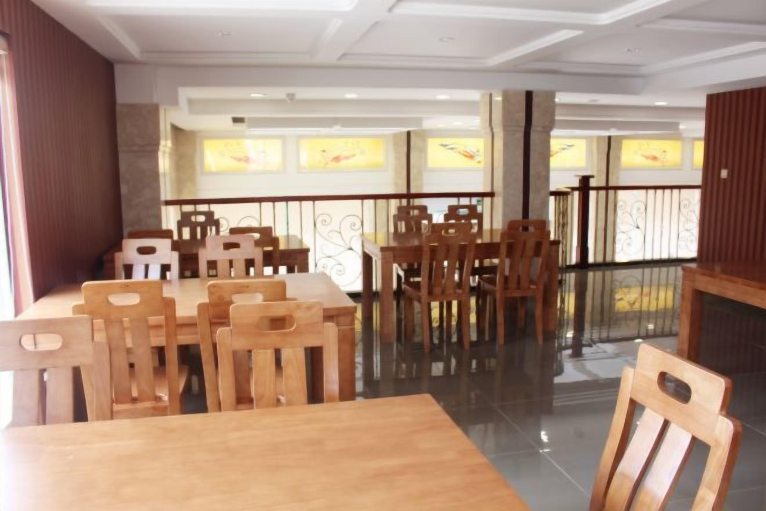 A dining area with wooden tables and chairs, a glass partition, and a view of the outside through windows.