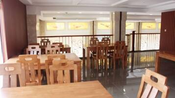 A dining area with wooden tables and chairs, a glass partition, and a view of the outside through windows.