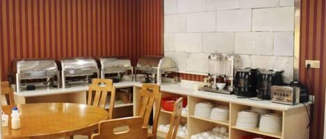 A breakfast area with a wooden table and chairs, buffet with food dispensers, and a coffee station.