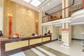A hotel reception area with a marble floor, a reception desk, a large decorative wall, and a staircase leading to an upper level. - NOMC Hotel (Xianju)