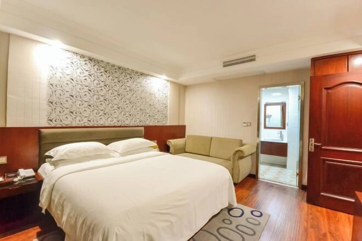 A hotel room with a bed, a nightstand, a sofa, and a door.