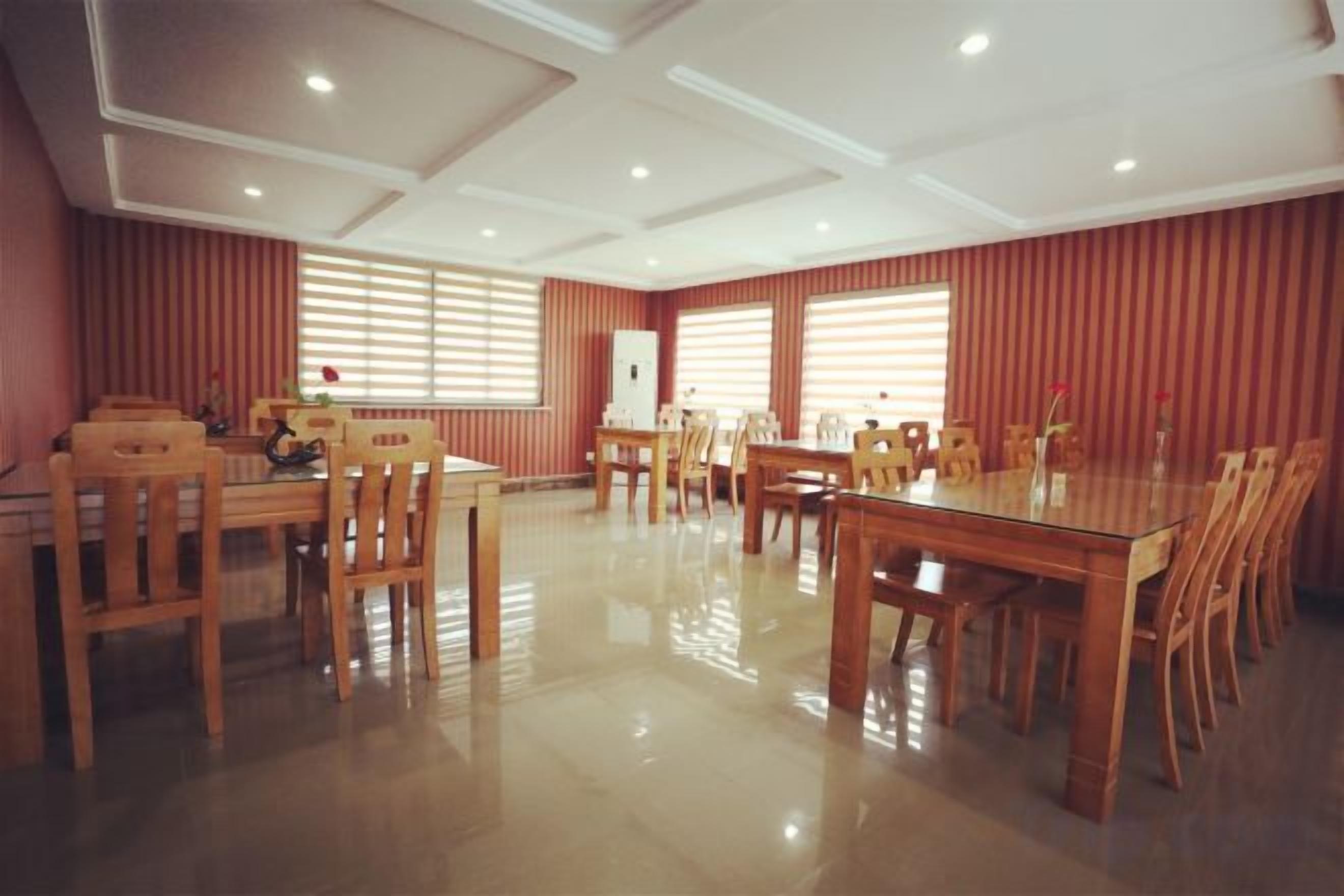 Un comedor amplio con varias mesas y sillas de madera, ventanas grandes con persianas y un techo alto con iluminación empotrada.